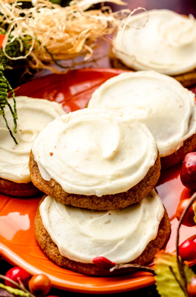 Frosted pumpkin cookies on a plate with fall decor all around.