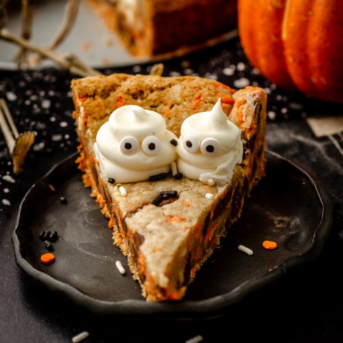 A slice of Halloween cookie cake with buttercream ghosts piped onto it on a black plate.