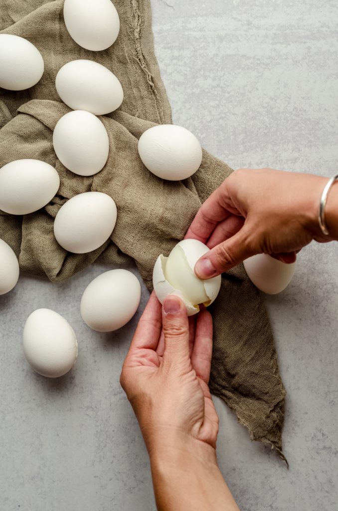 Aerial photo of hands holding and peeling a hard boiled egg.