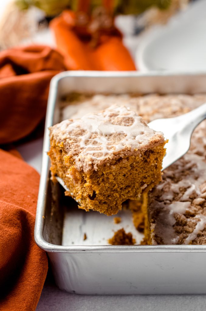 Someone is lifting a slice of pumpkin coffee cake out of a pan.
