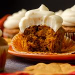 A pumpkin cupcake sitting on a plate with a bite taken out of it.