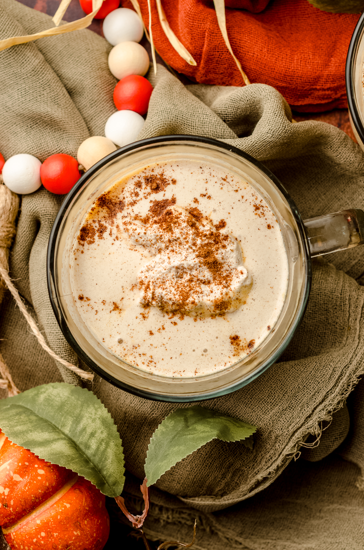 An aerial photo of pumpkin spice hot chocolate in a glass mug. There is pumpkin spice whipped cream and a sprinkle of cinnamon on top.
