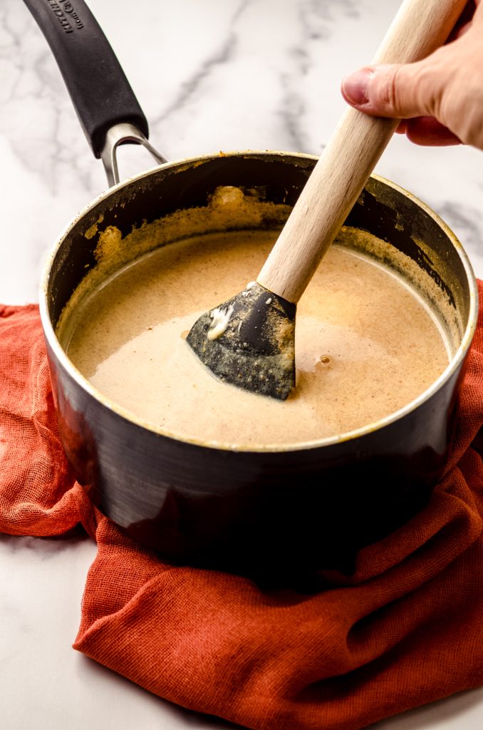 A saucepan of pumpkin spice hot chocolate with a spatula in it.
