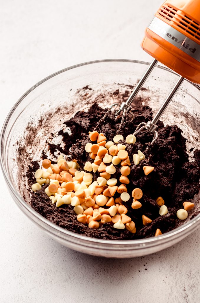 Chocolate Halloween cookie dough in a glass bowl with a handheld mixer.