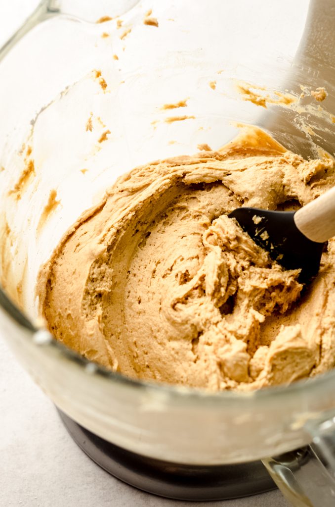 Peanut butter frosting in a large glass bowl with a spatula.