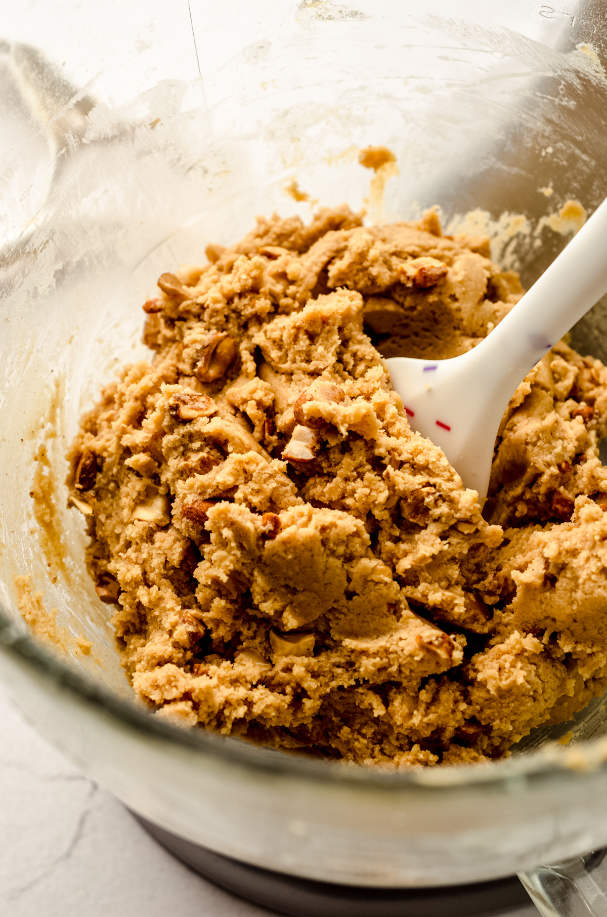 A large glass bowl of peanut butter cookie dough with a spatula in it.