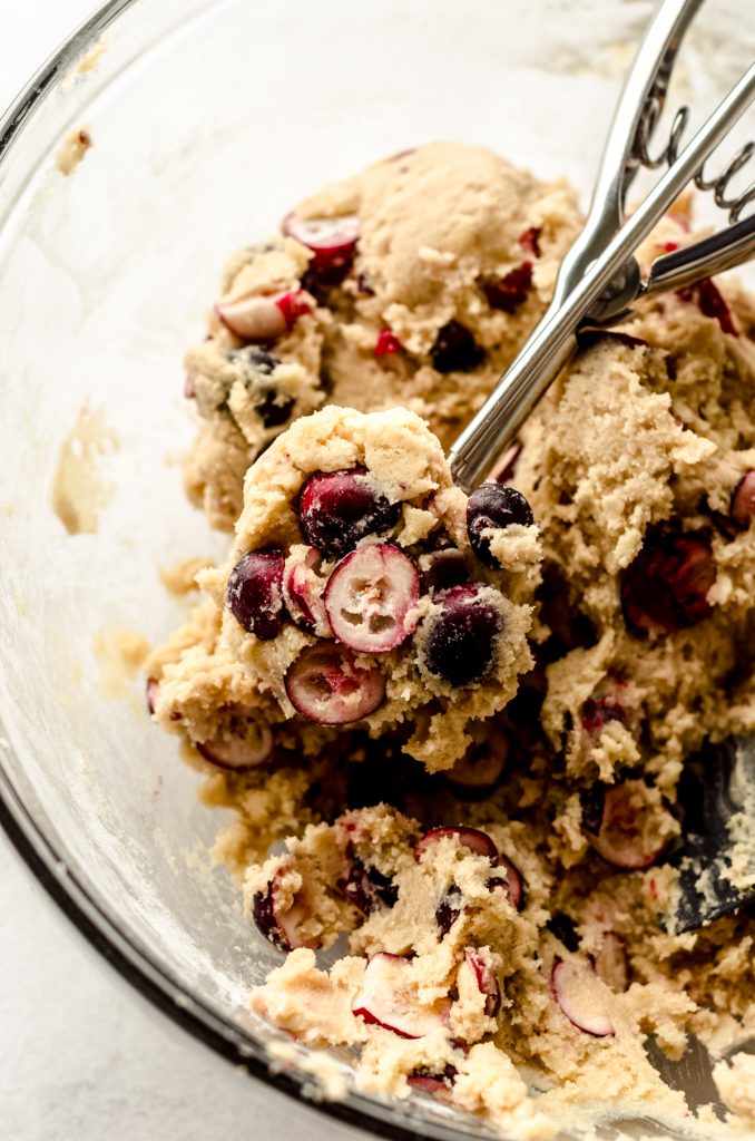 Fresh cranberry cookie dough in a bowl with a cookie scoop in it.