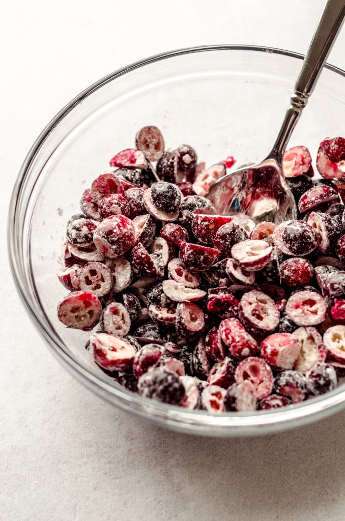 A bowl of chopped cranberries and flour with a spoon in it.