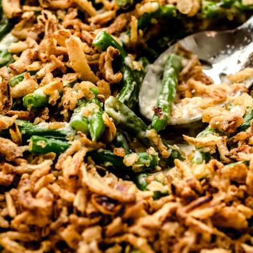 Green bean casserole without mushrooms in a baking dish with a serving spoon.