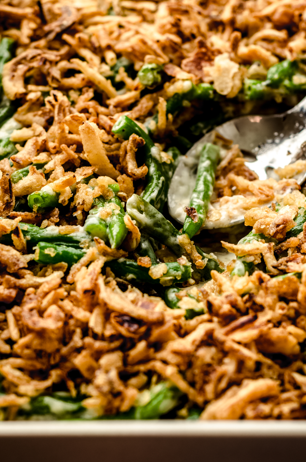 Green bean casserole without mushrooms in a baking dish with a serving spoon.