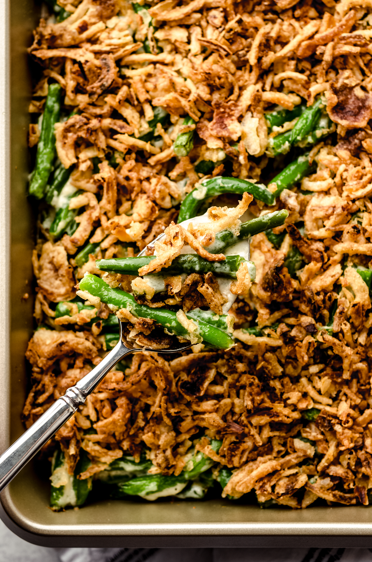 Green bean casserole without mushrooms in a baking dish with a serving spoon.