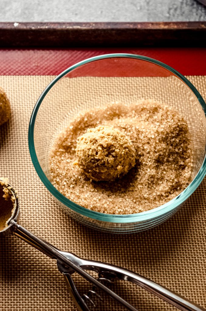 A gingersnap cookie dough ball in a bowl of coarse sugar for the coating.