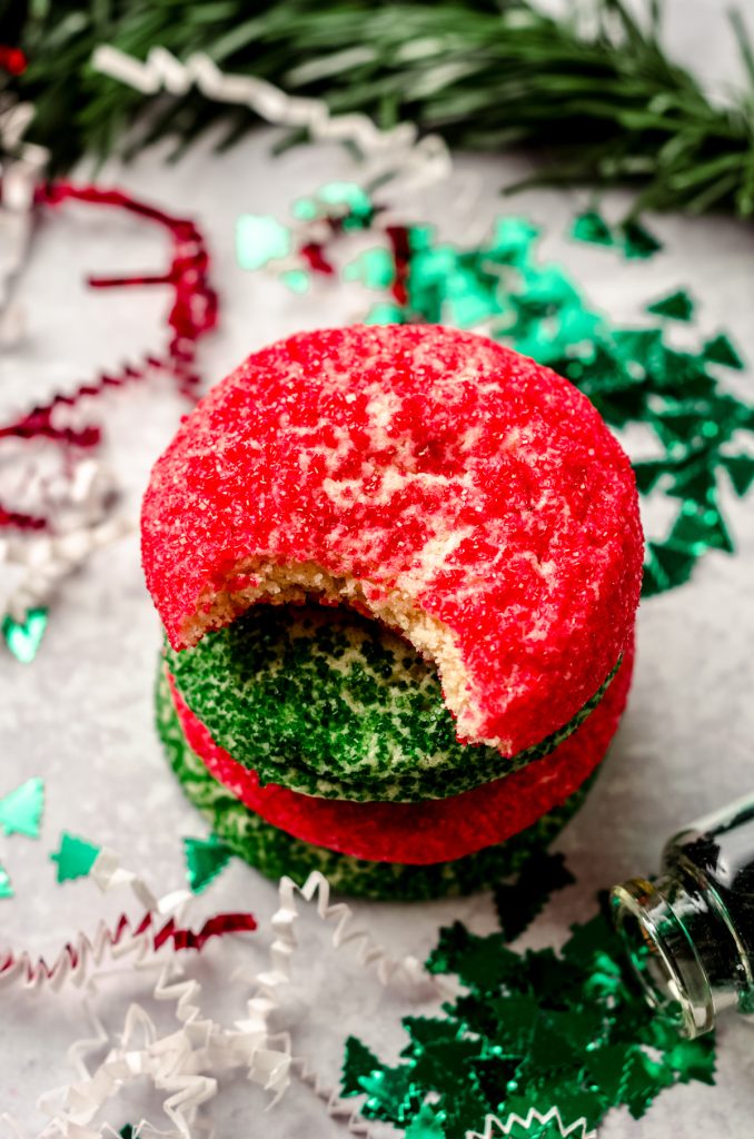 A stack of red and green Christmas sugar cookies. A bite has been taken out of the one on the top.