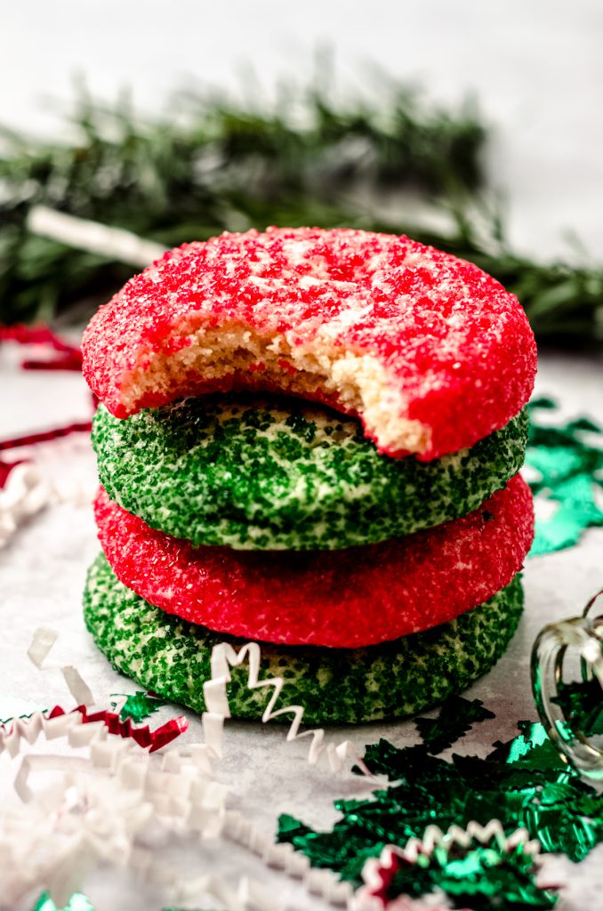 A stack of red and green Christmas sugar cookies. A bite has been taken out of the one on the top.