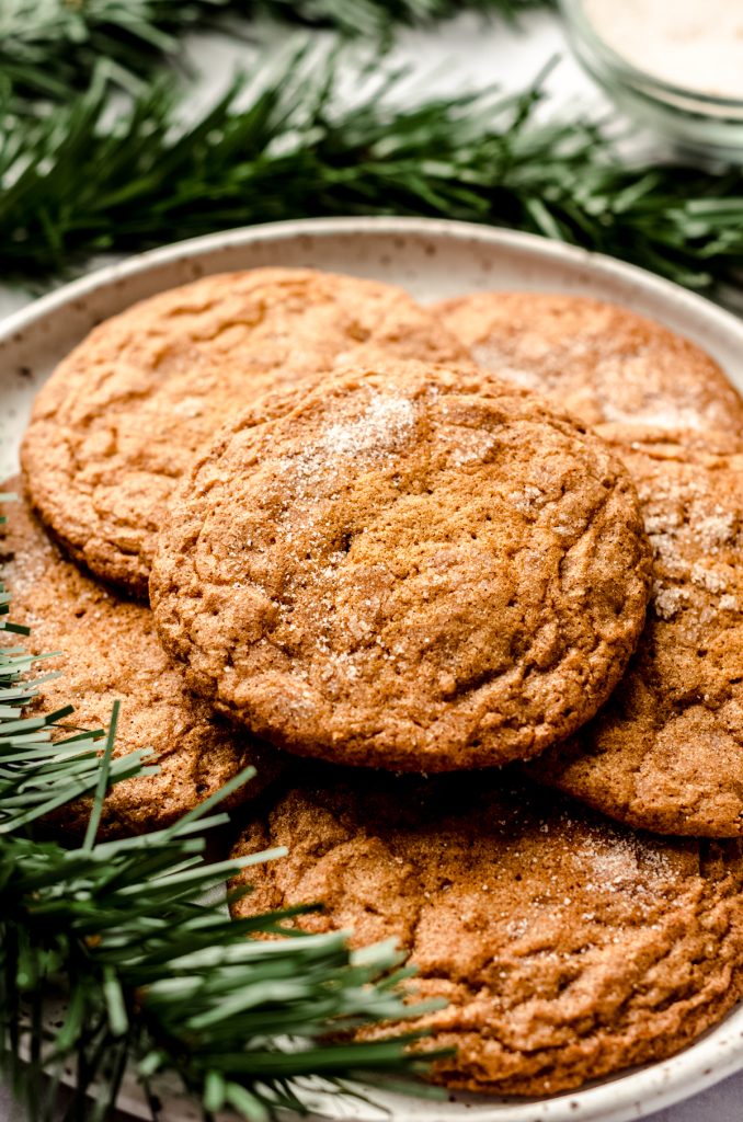 Spiced gingersnap cookies on a plate with evergreen accents around it.
