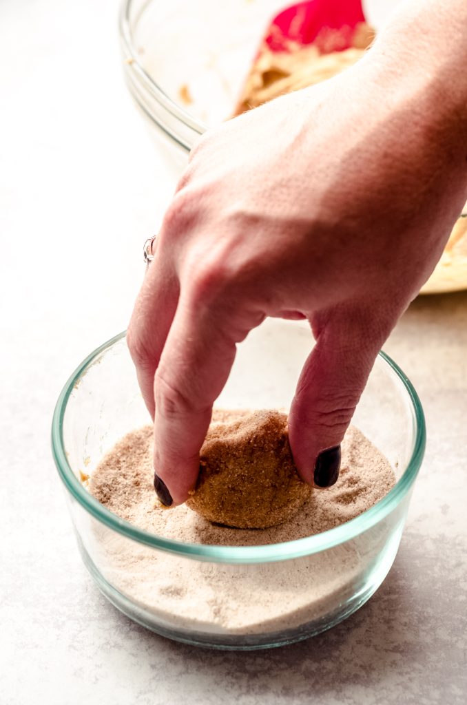 Someone is rolling a gingersnap cookie dough ball into a spiced sugar mixture.