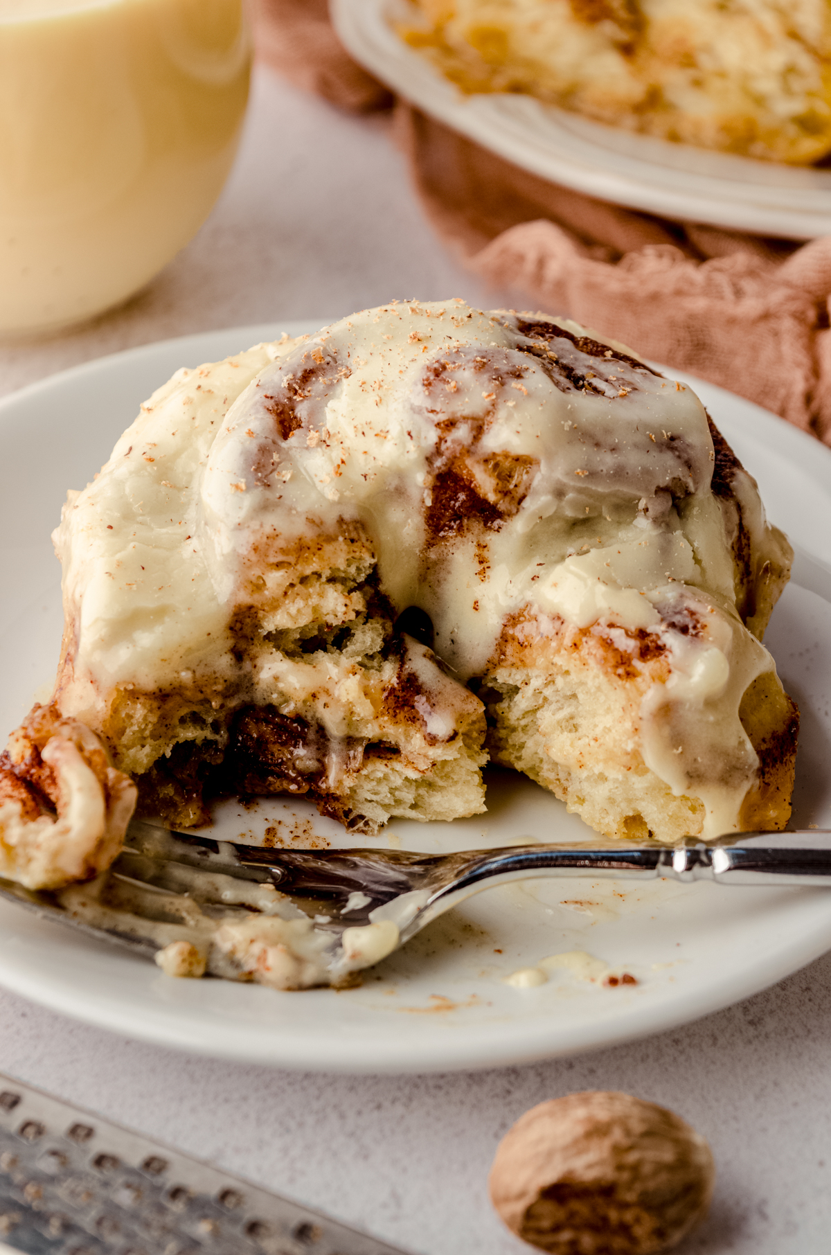 An eggnog cinnamon roll on a plate with a fork. A bite has been taken out of it.