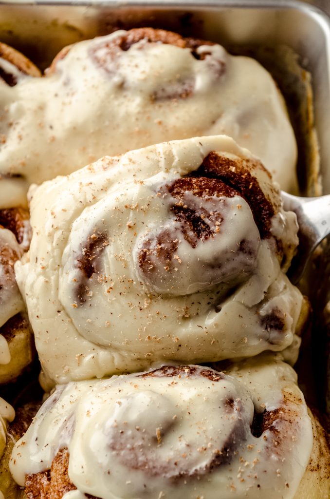 Eggnog cinnamon rolls in a baking dish with a spatula lifting one out.