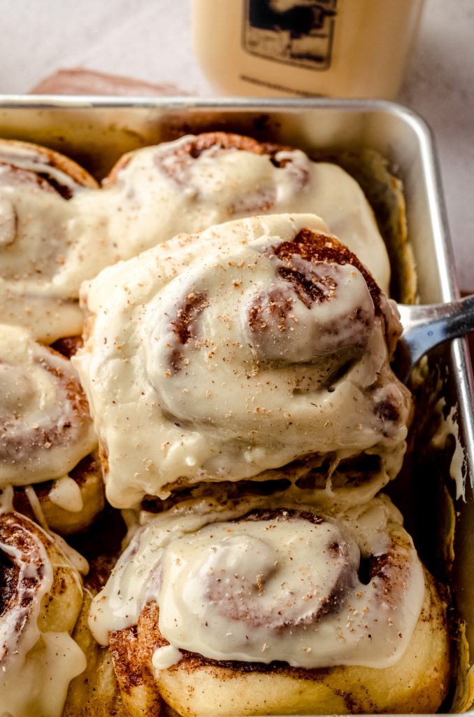 Eggnog cinnamon rolls in a baking dish with a spatula lifting one out.