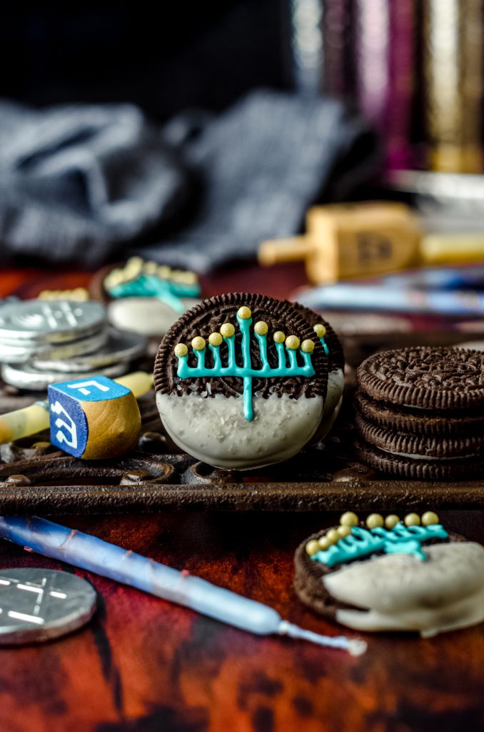 Hanukkah Oreos on a surface surrounded by candles and dreidels.