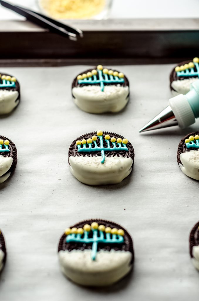 Hanukkah Oreos on a baking sheet with a piping bag in the background.