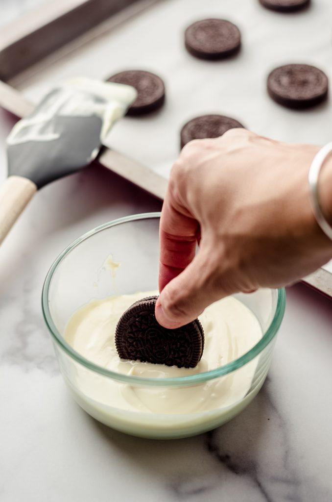 Someone is dipping an Oreo into a bowl of melted white chocolate.
