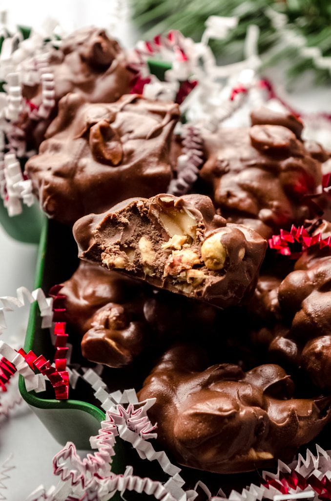 Peanut clusters in a Christmas tree shaped container with red and white confetti around it. A bite has been taken out of one of the clusters on top.