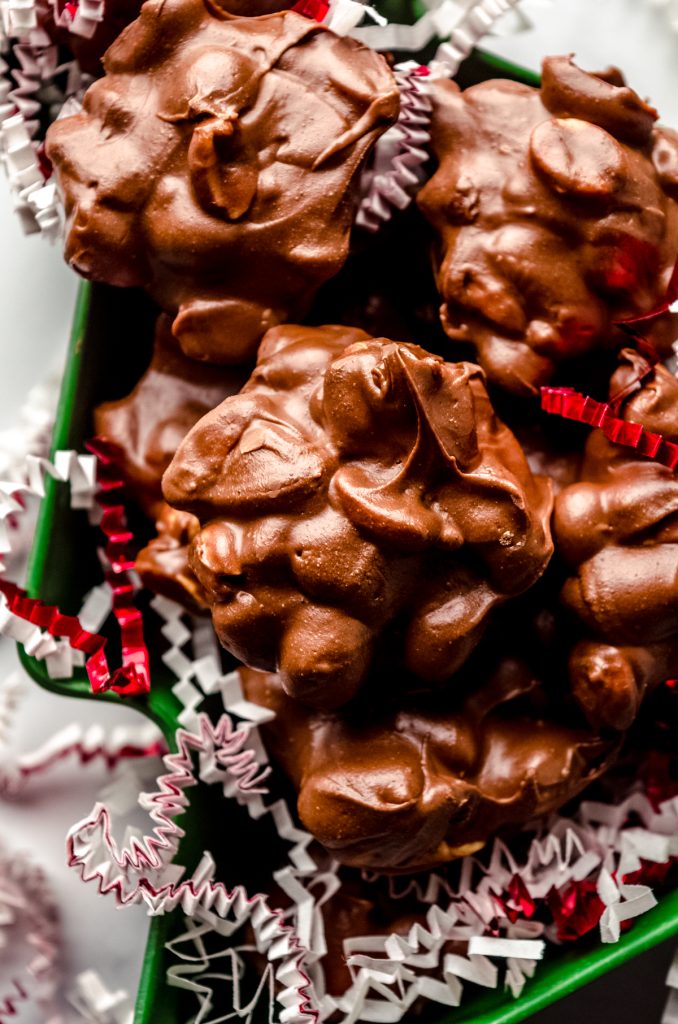 Peanut clusters in a Christmas tree shaped container with red and white confetti around it.