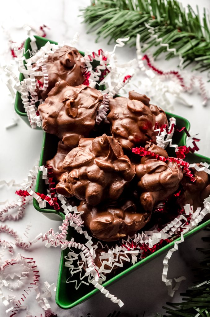 Peanut clusters in a Christmas tree shaped container with red and white confetti around it.