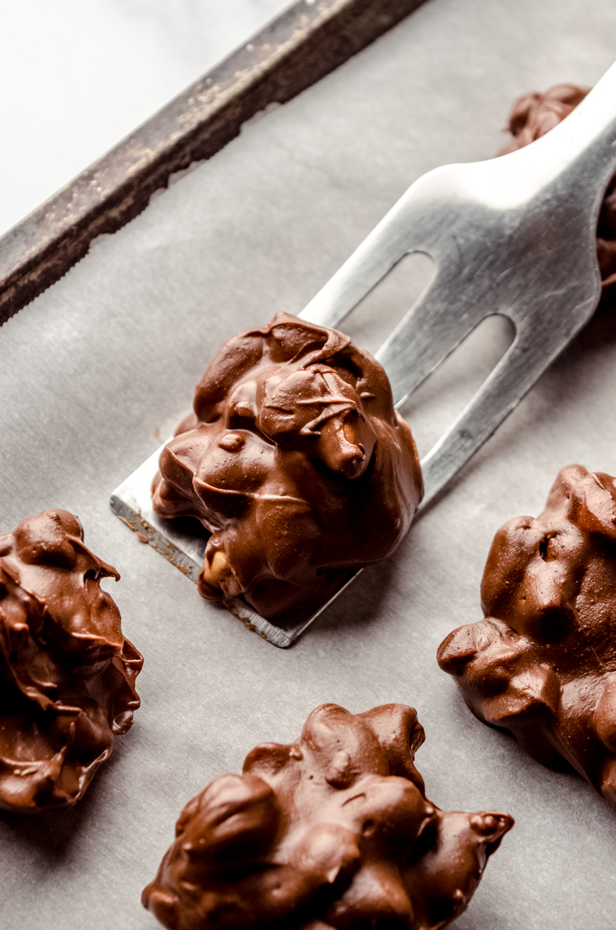 Someone is using a spatula to scoops peanut clusters from a baking sheet with parchment paper.