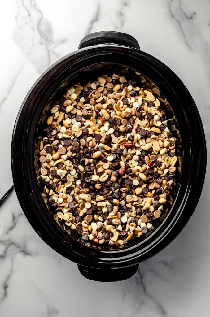 Peanuts, white chocolate chips, peanut butter chips, and semisweet chocolate chips mixed together in a slow cooker.