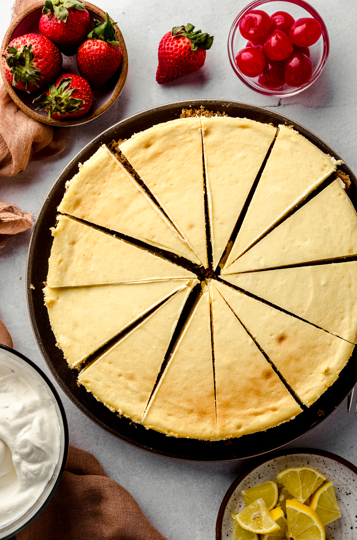 Aerial photo of a classic cheesecake that has been sliced. There are toppings all around it.