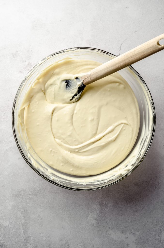 Classic cheesecake batter in a large glass bowl with a spatula.