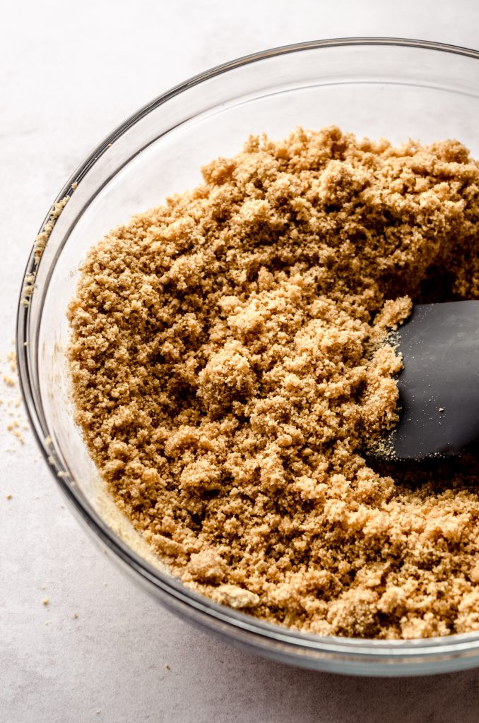 The mixture for a graham cracker crust in a bowl with a spatula.