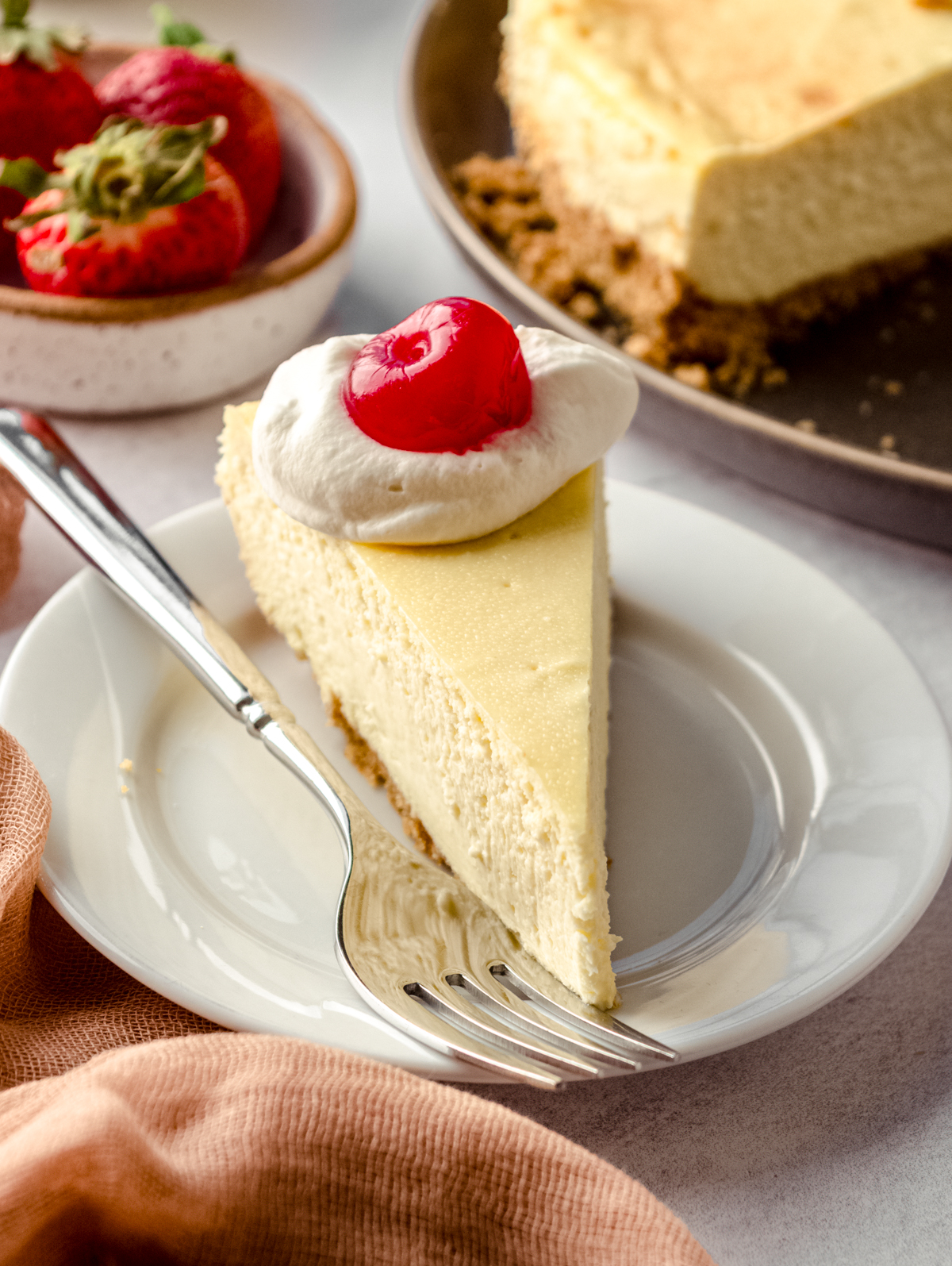 A slice of cheesecake on a plate. There is a dollop of whipped cream and a cherry on top of the slice.