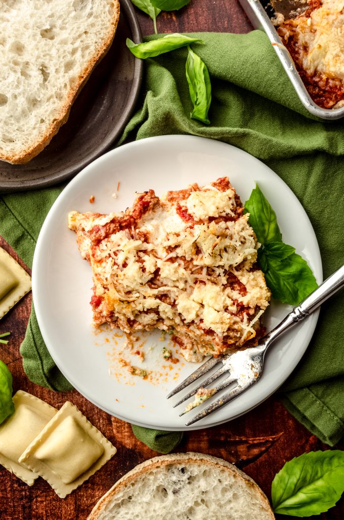 Aerial photo of a slice of ravioli lasagna on a plate with a fork and a bite has been taken out of it.