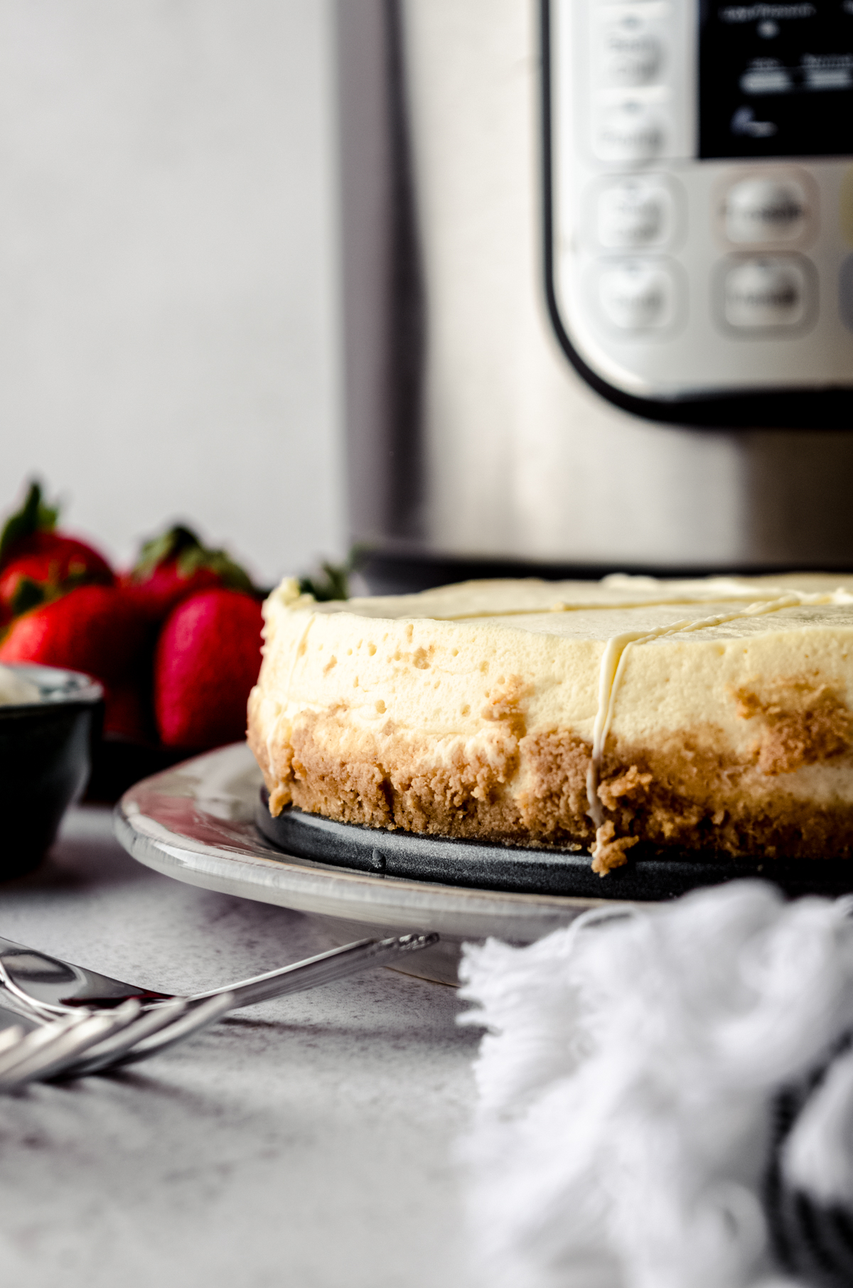 A cheesecake on a platter with an Instant Pot in the background.