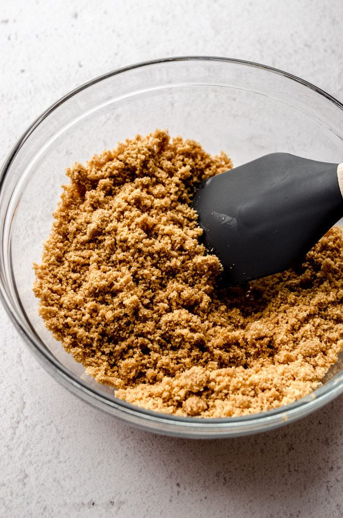 Ingredients for graham cracker crust for a cheesecake in a glass bowl with a spatula.