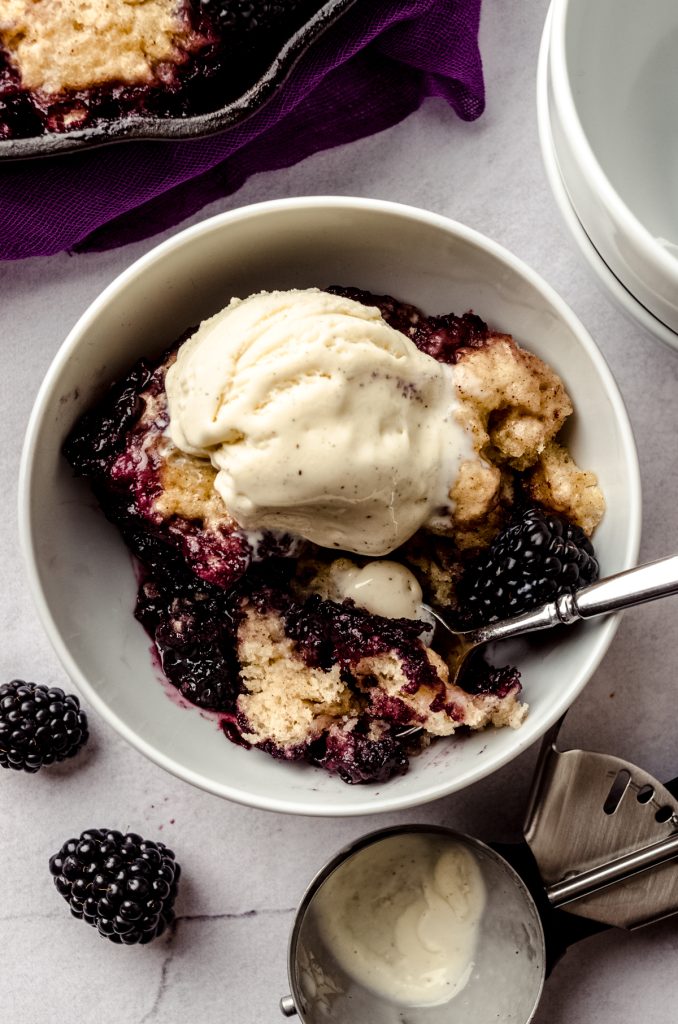Blackberry dumplings in a bowl with a spoon and a scoop of vanilla ice cream on tpo.