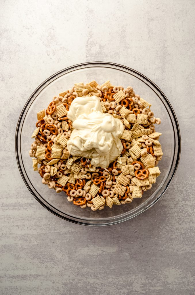 Cheerios, Chex, and pretzels in a large bowl with melted white chocolate poured on top.