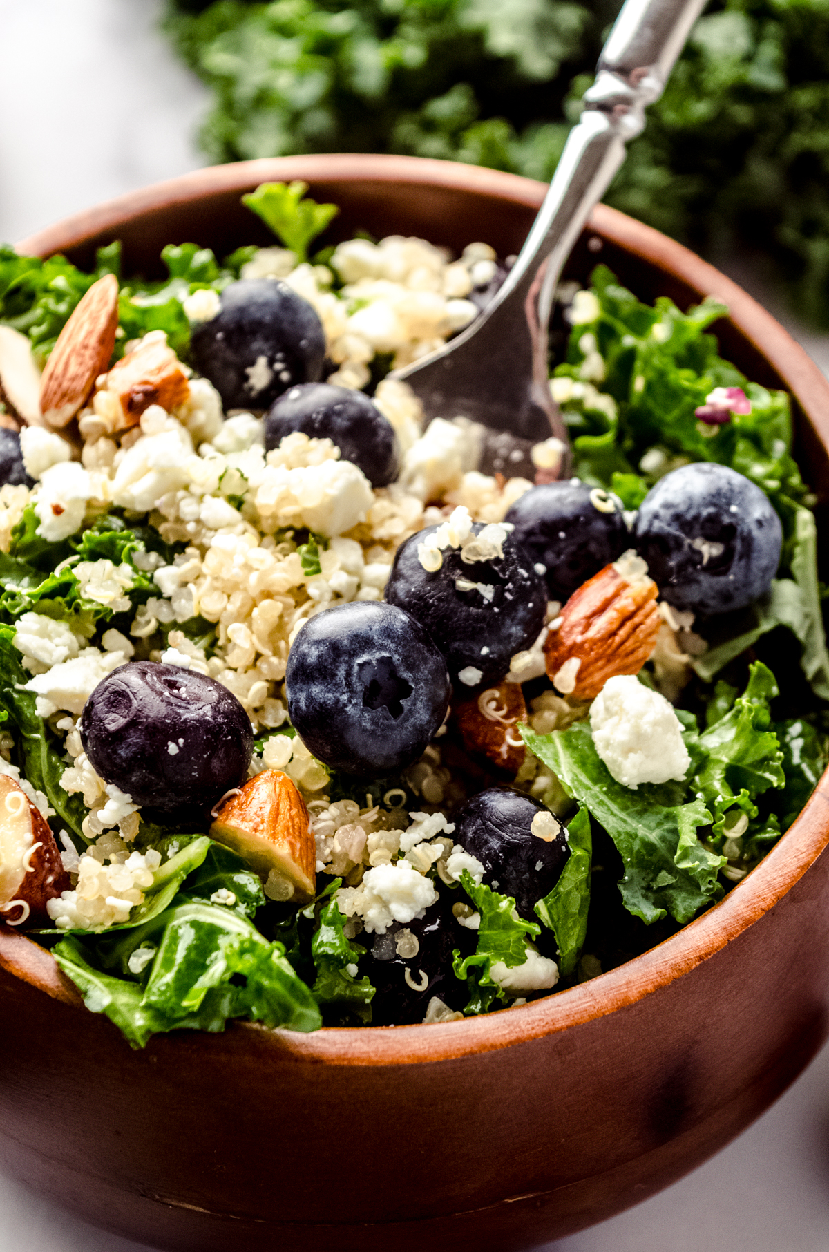 Blueberry quinoa kale salad in a small brown wooden bowl.