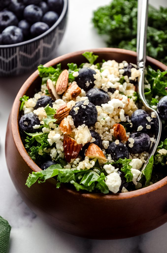 Blueberry quinoa kale salad in a small brown wooden bowl.