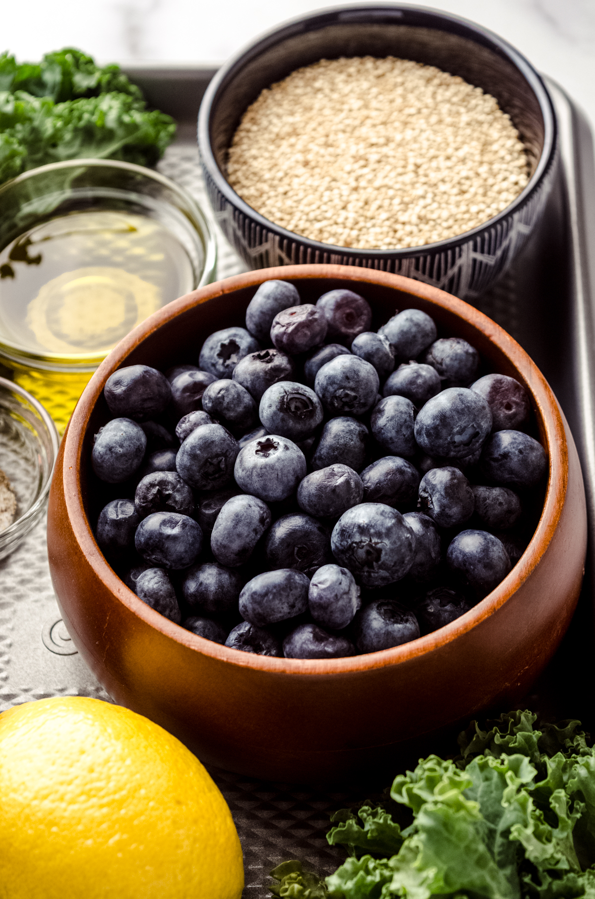 A bowl of blueberries on a surface with a lemon, quinoa, and olive oil in bowls around it.