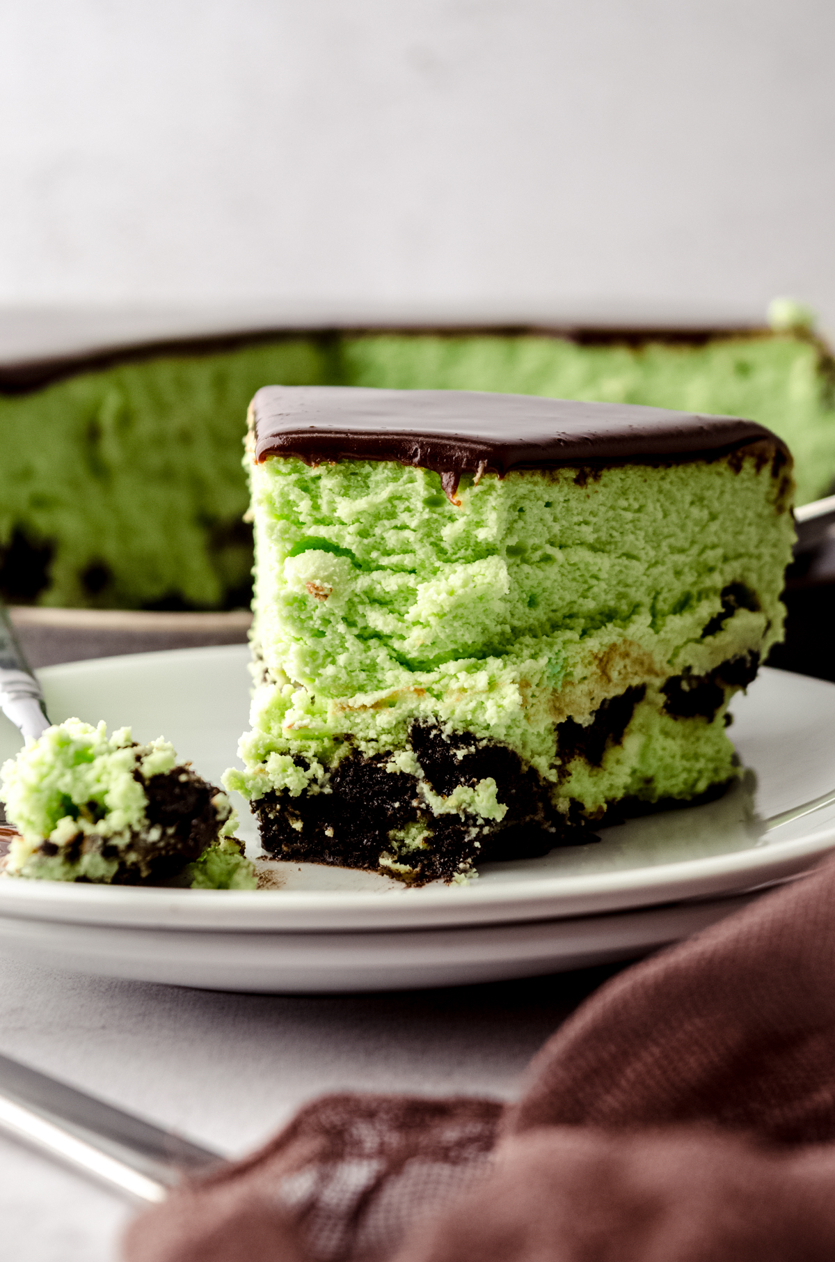 A slice of mint chocolate cheesecake on a plate with a fork. A bite has been taken out of it.