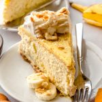 A slice of banana pudding cheesecake on a plate with a fork and some slices of bananas on the plate.