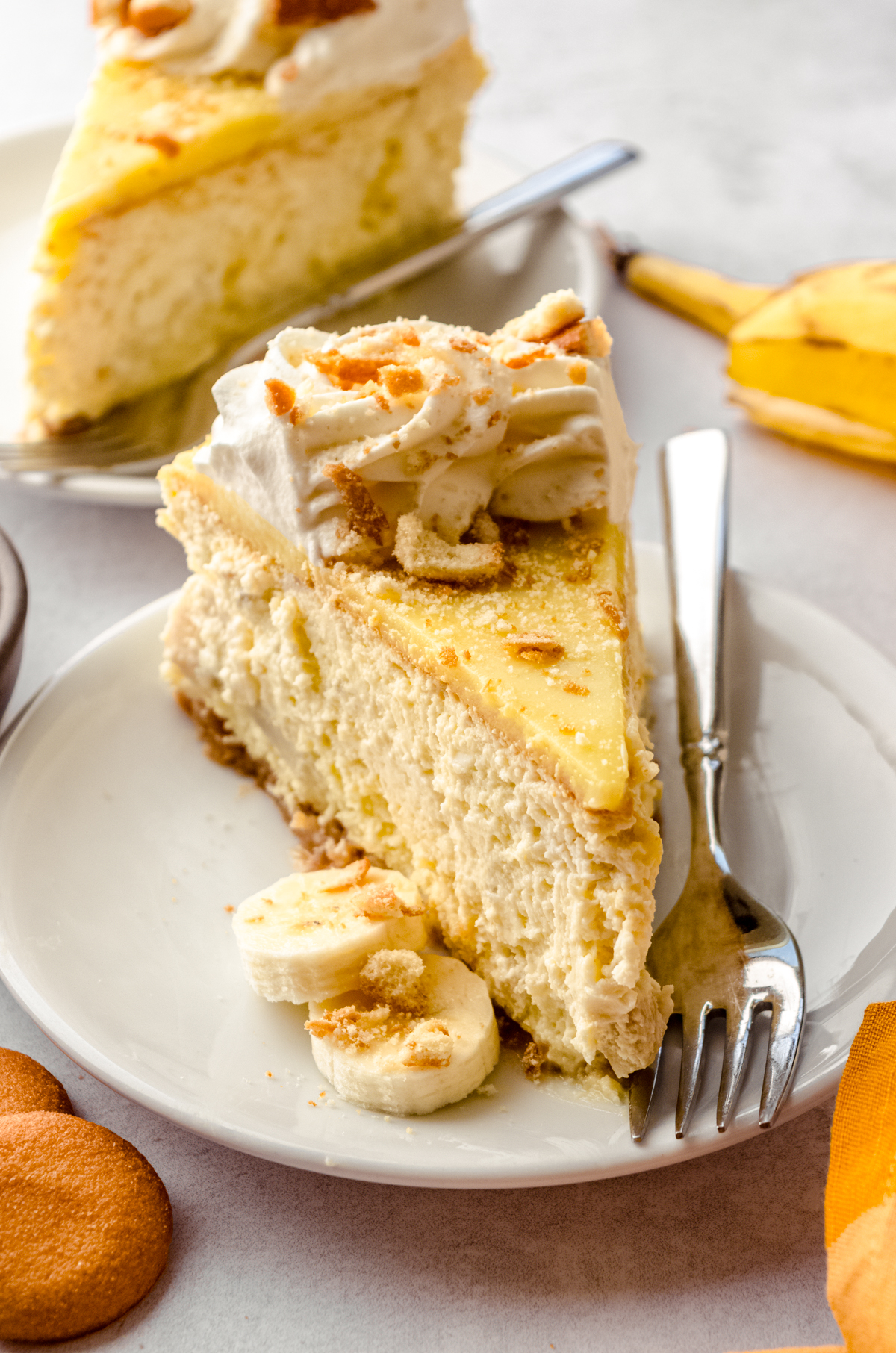 A slice of banana pudding cheesecake on a plate with a fork and some slices of bananas on the plate.