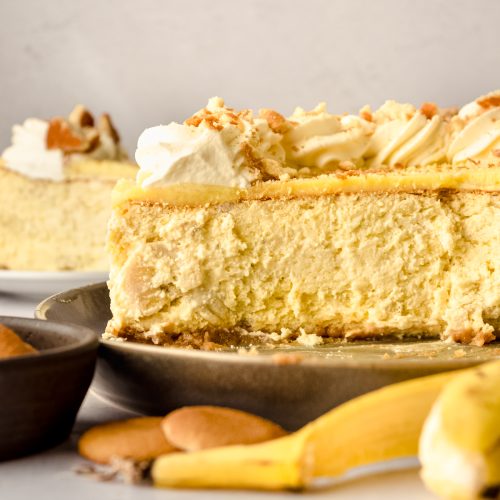 The cross-section of a banana pudding cheesecake on a plate with Nilla Wafers and a banana peel in the foreground.