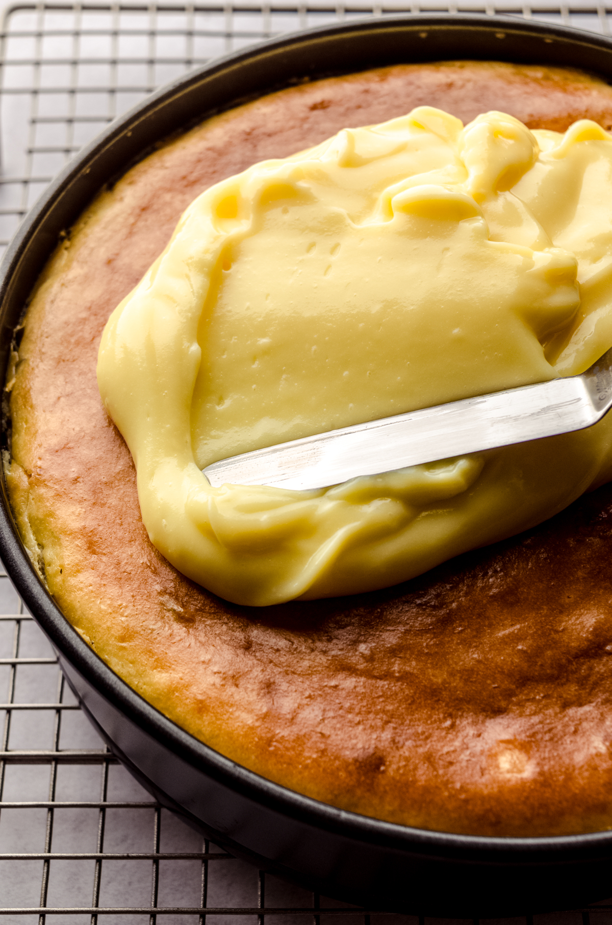 Someone is using an offset spatula to spread vanilla pudding onto the top of a banana pudding cheesecake.