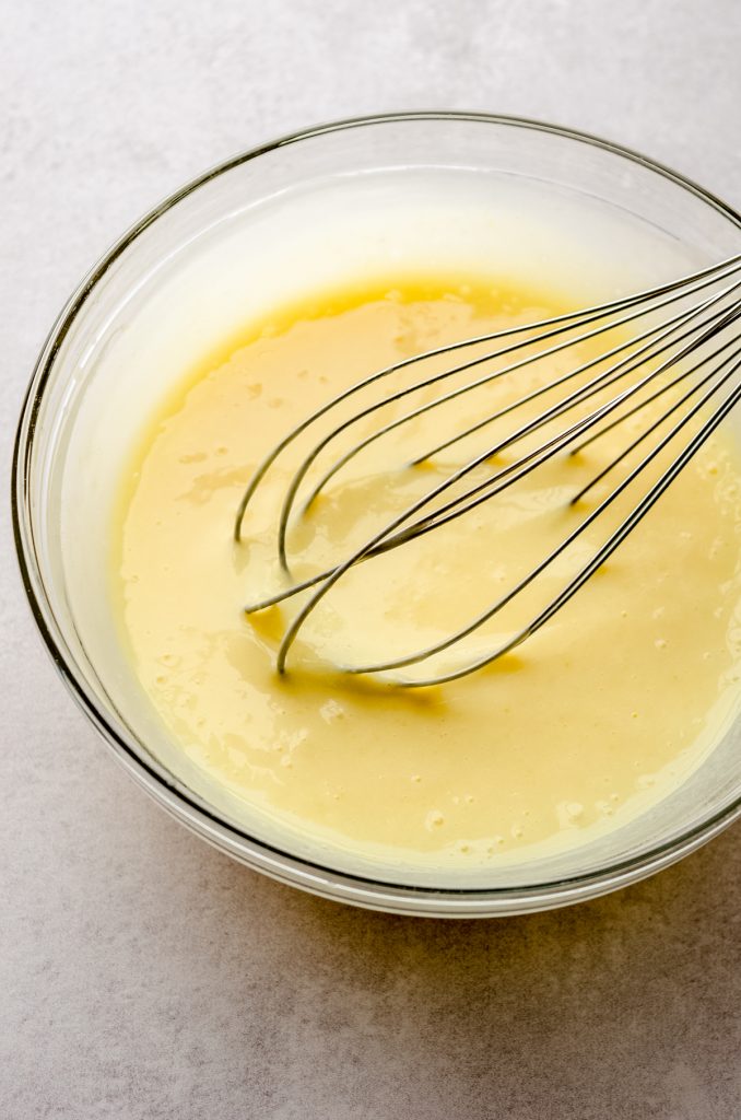 A bowl of vanilla pudding with a whisk in it.