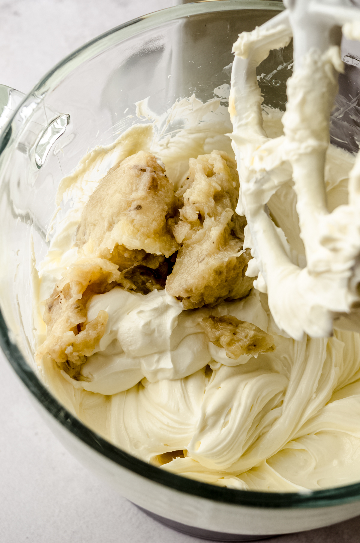 The bowl of a stand mixed filled with cheesecake filling and mashed roasted bananas dropped into the batter.